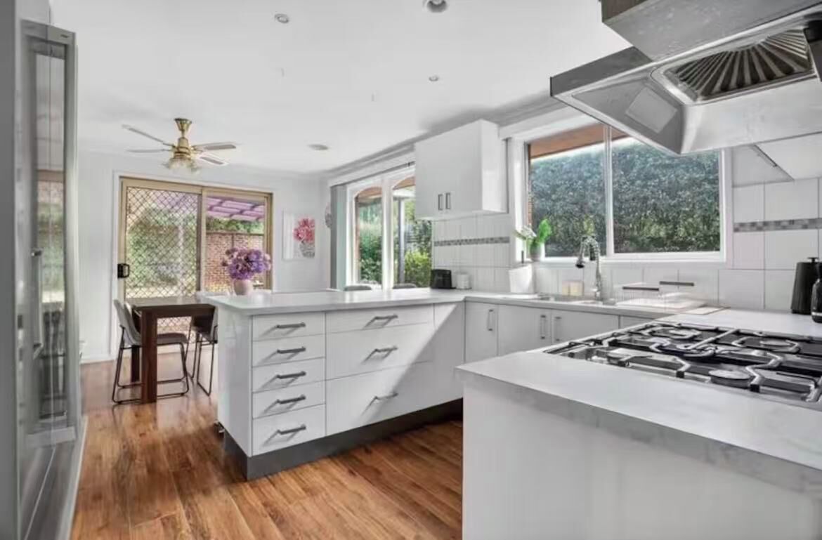 A modern kitchen with white cabinetry, a large island with a gas stove, and a dining area with a table and chairs.