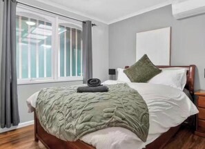 A bedroom with a bed, a window with curtains, a bedside table, and a wall-mounted light fixture. - 4B cozy holiday house by frankston sea (Frankston)