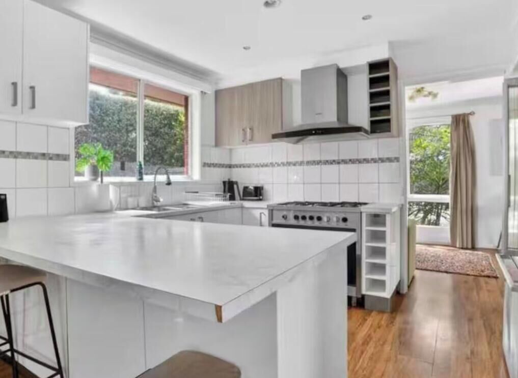 Una cocina moderna con una isla grande, muebles blancos y vistas al exterior.
