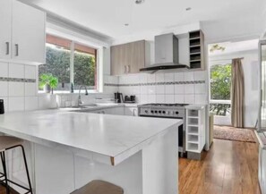 A modern kitchen with a large island, white cabinetry, and a view of the outdoors. - 4B cozy holiday house by frankston sea (Frankston)
