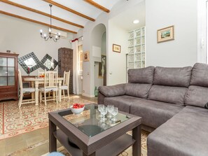 Ein Wohnzimmer mit Sofa, einem Glastisch, einem Esstisch mit Stühlen, einer Kristallleuchtre und einem Schrank.