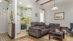A living room with a grey sofa, a small table, and a chair. There is a kitchen in the background with a stove and cabinets. - Poble Nou - Llacuna by Interhome (Barcelona)