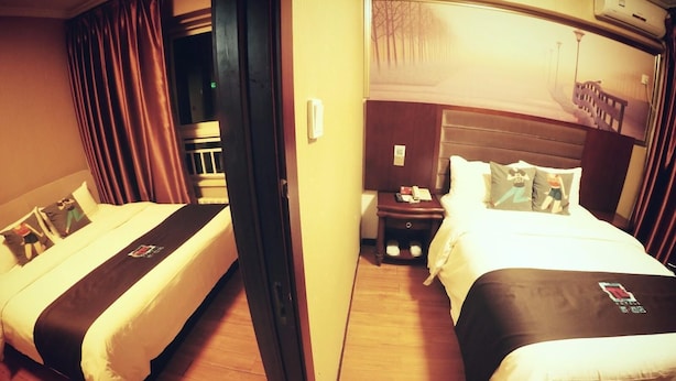 Ein Hotelzimmer mit zwei Betten, Holzboden, einem Nachttisch mit Telefon und einem Fenster mit Blick auf Bäume.