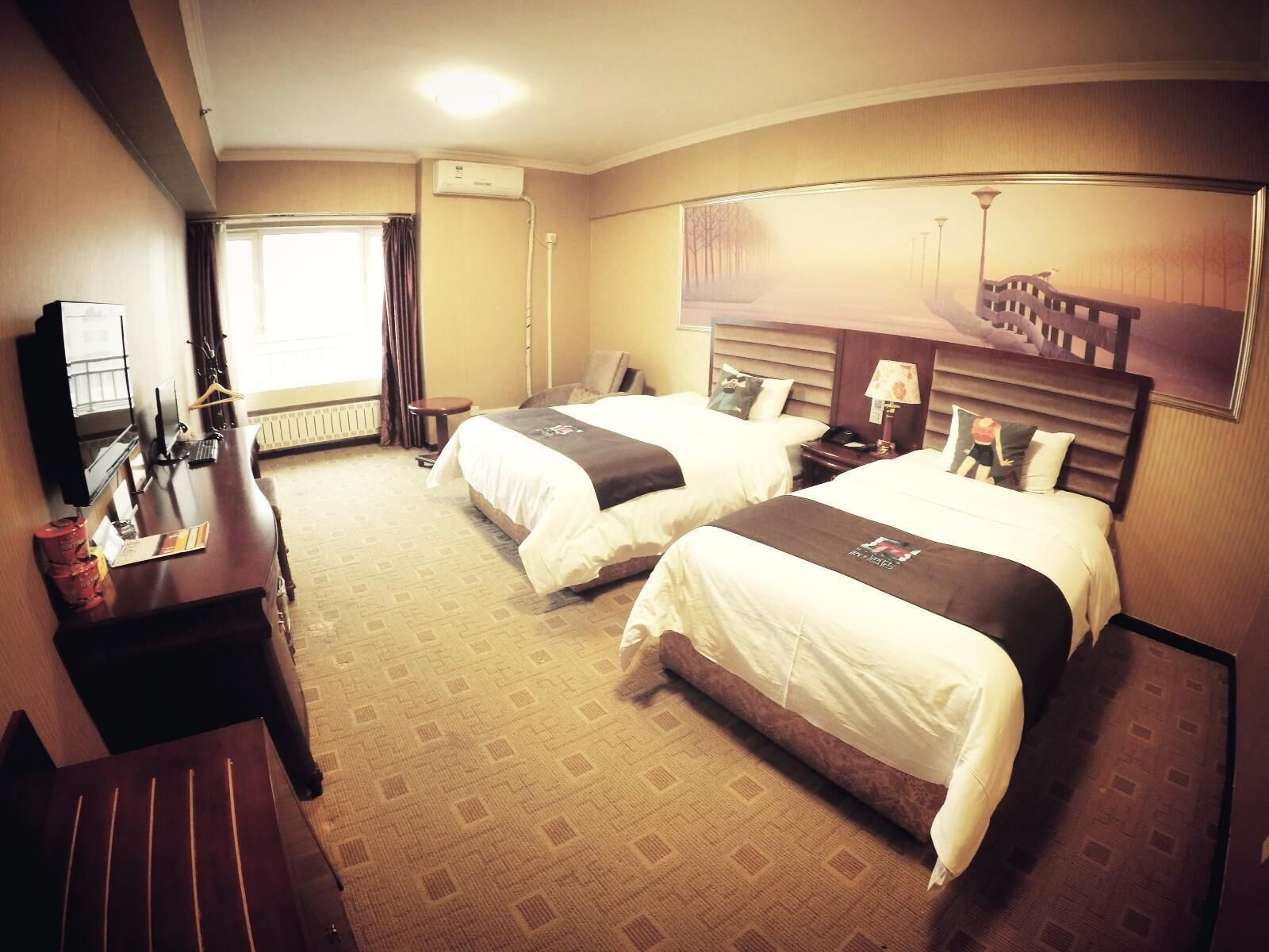 A hotel room with two beds, a desk, a TV, and a window with curtains.