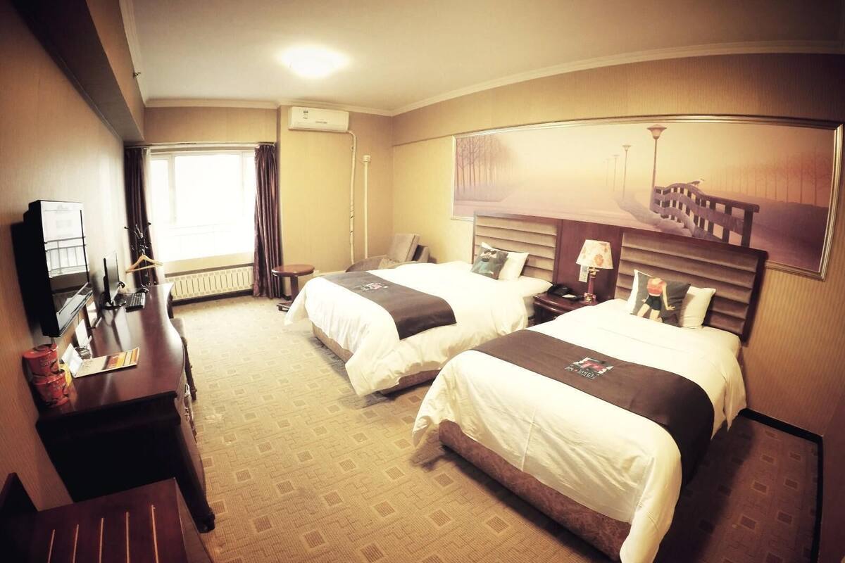 Habitació d'hotel amb dos llits, una taula de treball, televisió i una finestra amb cortines.