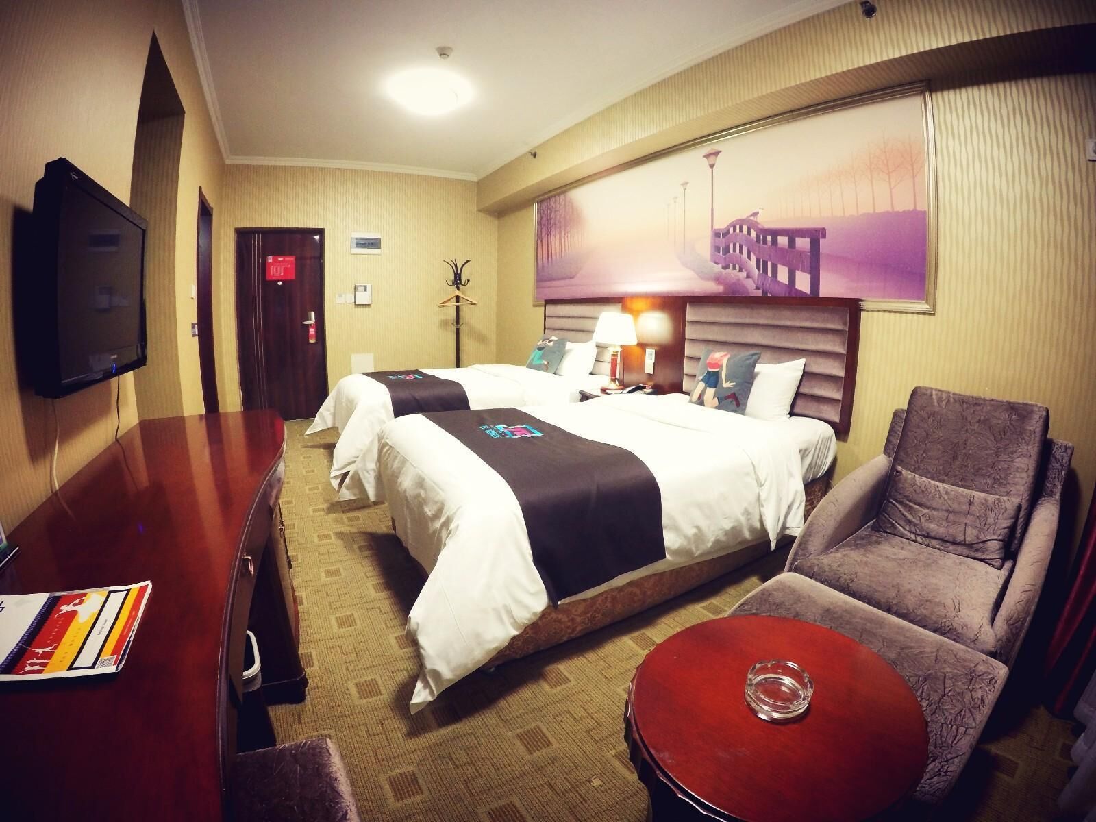 A hotel room with two beds, a TV, a desk, a chair, and a painting on the wall.