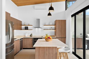 Eine moderne Küche mit Holzausstattung, einem Edelstahlkühlschrank, einem eingebauten Backofen und einer Kochinsel mit Obstschale.