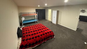 A room with bunk beds, a single bed with a red and black checkered bedspread, a wardrobe, and a door leading to a bathroom.