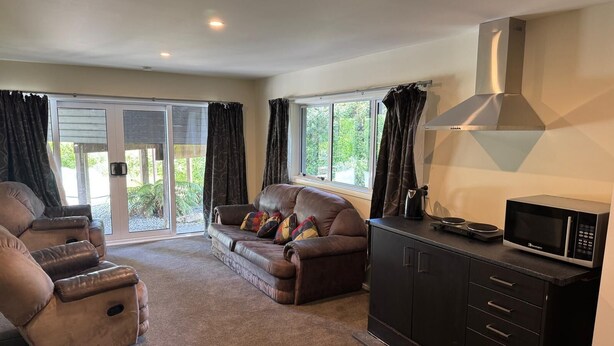 A living room with a sofa, a recliner, a kitchen area with a microwave, and a sliding glass door leading to an outdoor area.