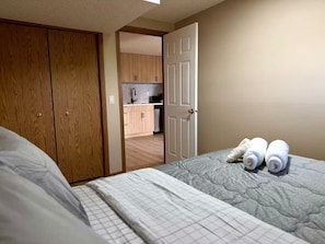A bedroom with a bed, a wooden wardrobe, and a door leading to a kitchen. - Spacious and private one bedroom apartment located in hidden valley. (Calgary)