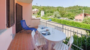 Un balcón con una mesa y sillas, una silla azul, y vista a un paisaje verde con edificios.