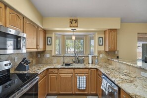 Una cocina con encimeras de granito, armarios de madera, electrodomésticos de acero inoxidable, una ventana con persianas y una lámpara colgante.