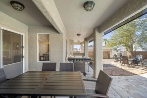 Un patio al aire libre con mesa y sillas, una parrilla y vistas al jardín trasero.