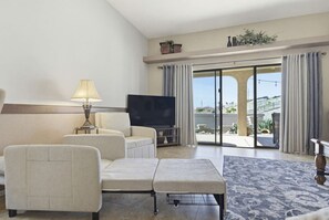 Un salon comprenant un canapé, un téléviseur, une lampe et une vue sur l’extérieur, accessible par une porte vitrée.