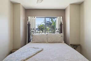 A bedroom with a bed, a window with curtains, a view of greenery, and a small table. - Villa Palmas - Pool, Comfort, Parking, ProjectorTV (Lake Havasu City)
