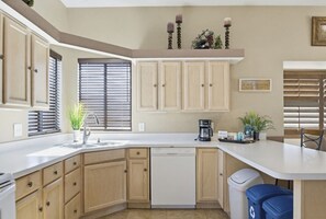 Une cuisine avec des meubles de rangement en bois, un lave-vaisselle, une machine à café et une poubelle.