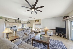 A modern living room with a sofa, coffee table, and TV. There is a kitchen area with cabinets and appliances. - Villa Palmas - Pool, Comfort, Parking, ProjectorTV (Lake Havasu City)