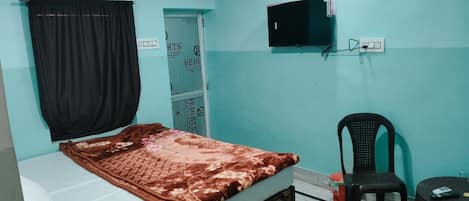 A room with a bed, a TV mounted on the wall, a chair, and a small table.