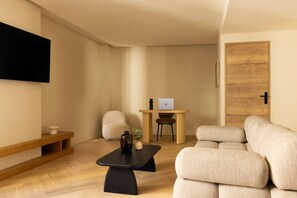 A modern living room with a sofa, a coffee table, a TV mounted on the wall, a wooden door, and a desk with a laptop. - Modern Appartement a/c 2br/4p - Montmartre (Paris)