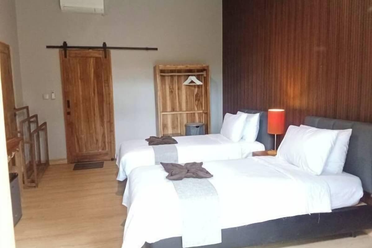 Habitación de hotel con dos camas, un armario de madera, una lámpara roja y una puerta de madera.