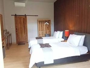 Hotellihuone, jossa on kaksi sänkyä, puinen vaatekaappi, punainen lamppu ja puinen ovi.