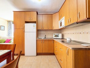 Eine kleine Küche mit Holzausstattung, einem weißen Kühlschrank, einer Mikrowelle und einem Spülbecken.