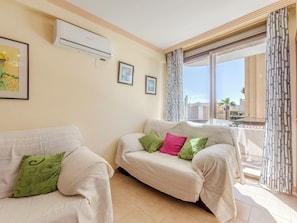 Ein Wohnzimmer mit zwei Sofas, einem großen Fenster mit gemusterten Vorhängen und einer Klimaanlage an der Wand.