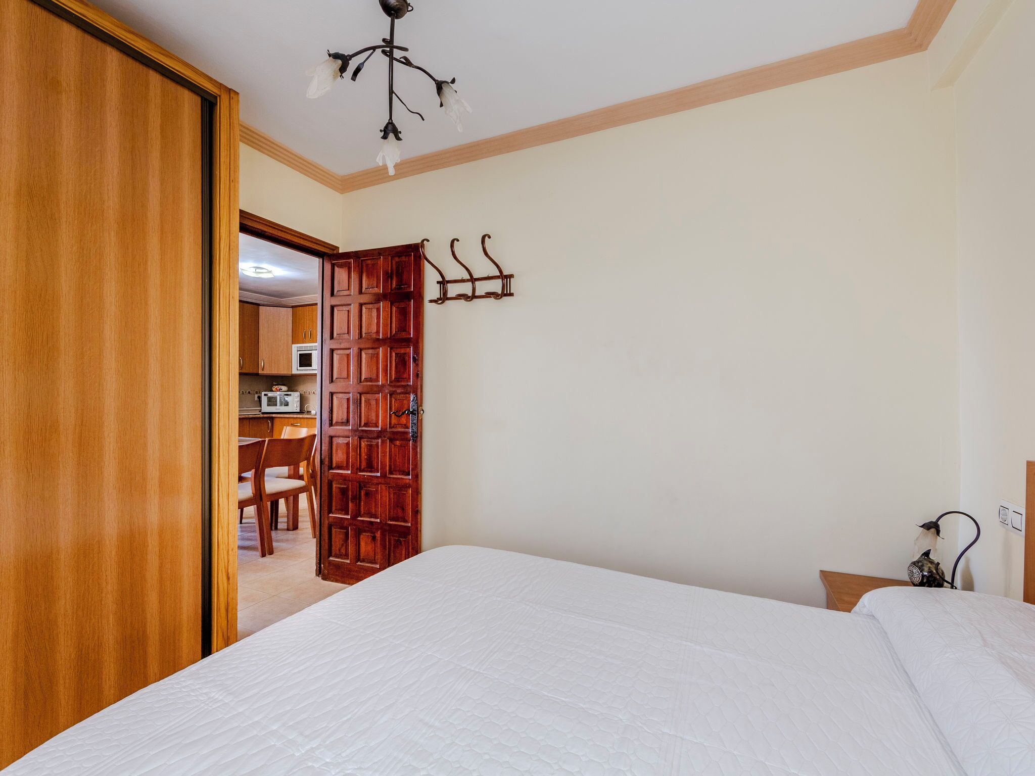 A bedroom with a bed, wooden wardrobe, and a kitchenette in the background.