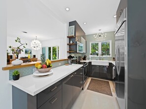 A modern kitchen with a central island, stainless steel appliances, and a view of greenery outside. - New, Mid-Century Modern Heated Private Pool Retreat Near Beaches & Dining! (Wilton Manors)