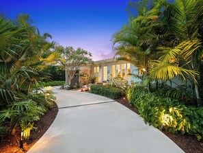 A house with a concrete pathway leading to the entrance, surrounded by lush greenery and palm trees. - New, Mid-Century Modern Heated Private Pool Retreat Near Beaches & Dining! (Wilton Manors)
