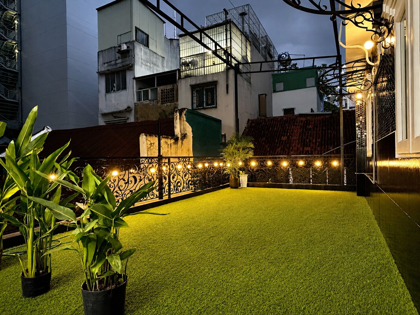 Una azotea con césped artificial, plantas en macetas y luces colgantes.