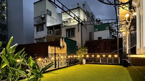 Terraço com grama sintética, plantas em vasos e luzes de cordão.
