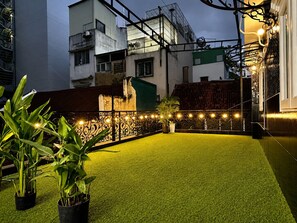 Terrat amb gespa artificial, plantes en testos i llums penjades.