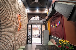 A brick-walled corridor with a ceiling fan, a table with a vase of flowers, and a view of parked scooters outside.