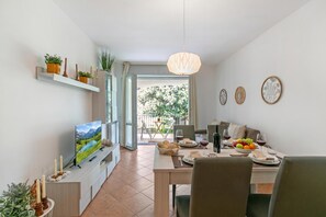 Ein moderner Essbereich mit Fernseher, Esstisch, Stühlen und Blick ins Freie.