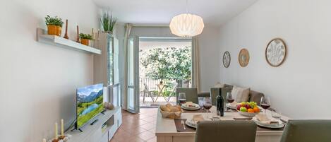 A modern dining area with a TV, dining table, chairs, and a view of the outdoors.