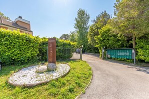 Ein verschlossenes Tor mit einem Schild, ein Kiesweg und ein Heckenstreifen.