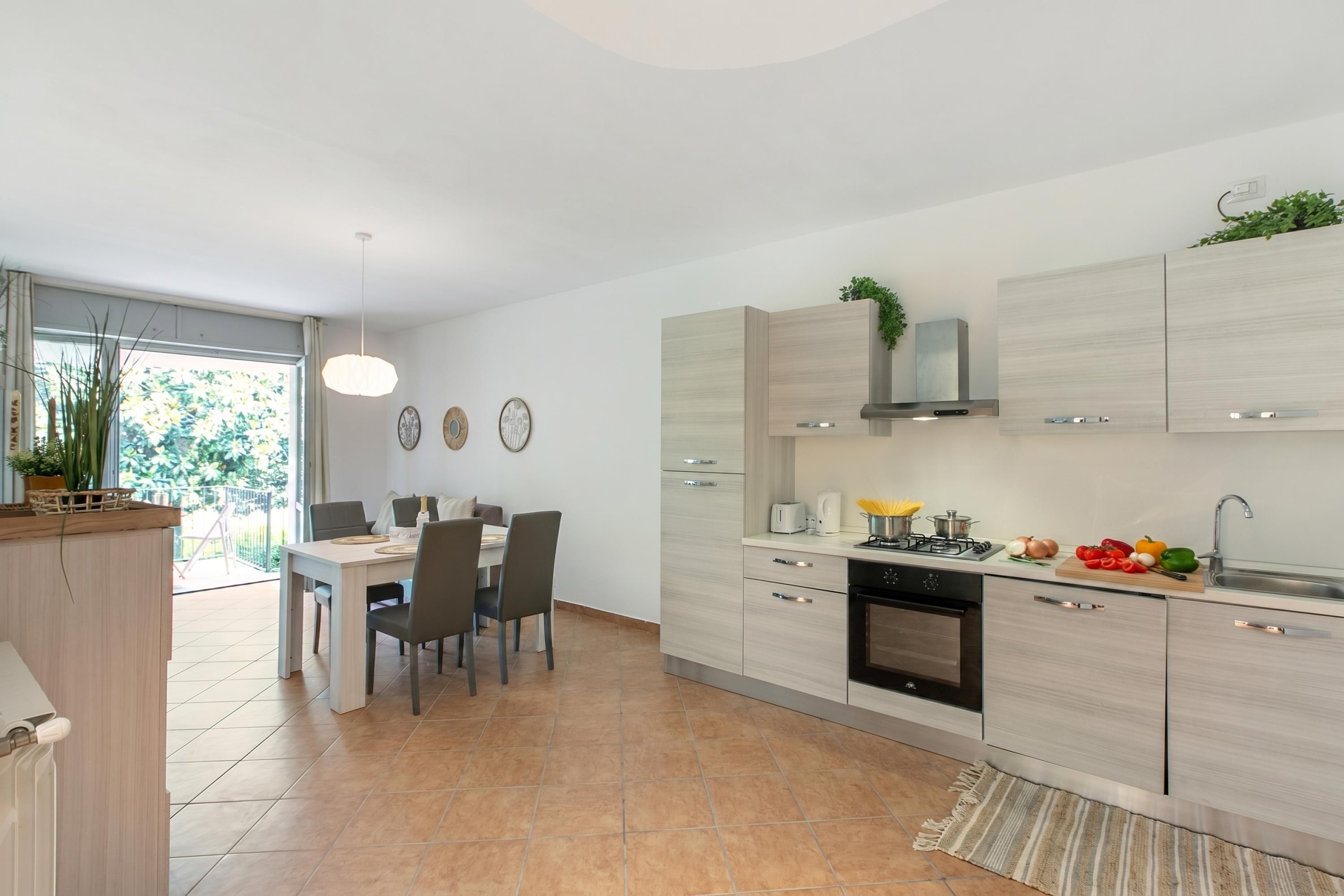 A modern kitchen with a dining area, featuring a built-in oven, a sink, and a countertop with fresh vegetables.
