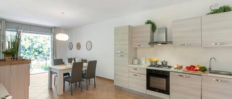 A modern kitchen with a dining area, featuring a built-in oven, a sink, and a countertop with fresh vegetables.
