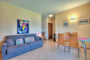 A living room with a sofa, a dining table with chairs, a ceiling light, and a door in the background. - Appartamento Lake View Laveno 1br, Sleeps 4 (Laveno Mombello)