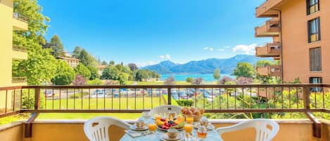 Un balcón con una mesa dispuesta para el desayuno, con vistas a un paisaje montañoso y un lago.