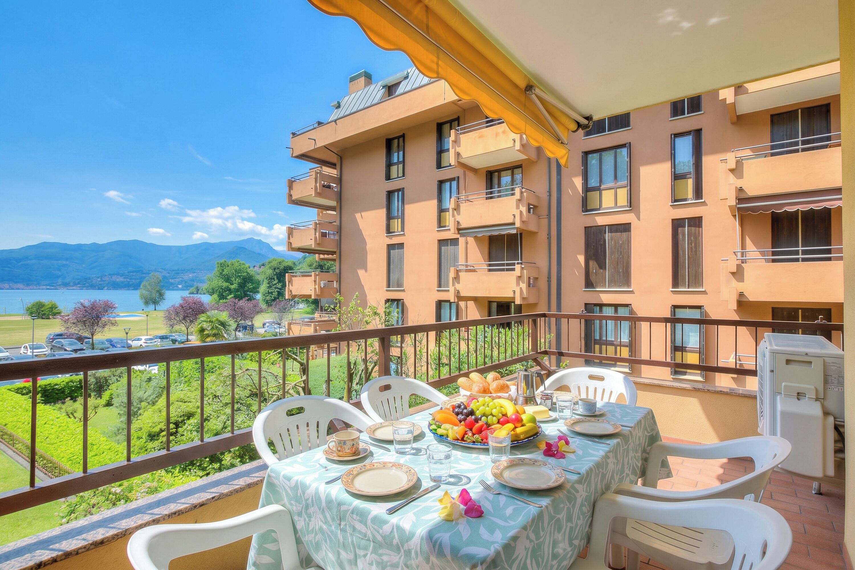 A balcony with a table set for dining, overlooking a body of water and mountains.