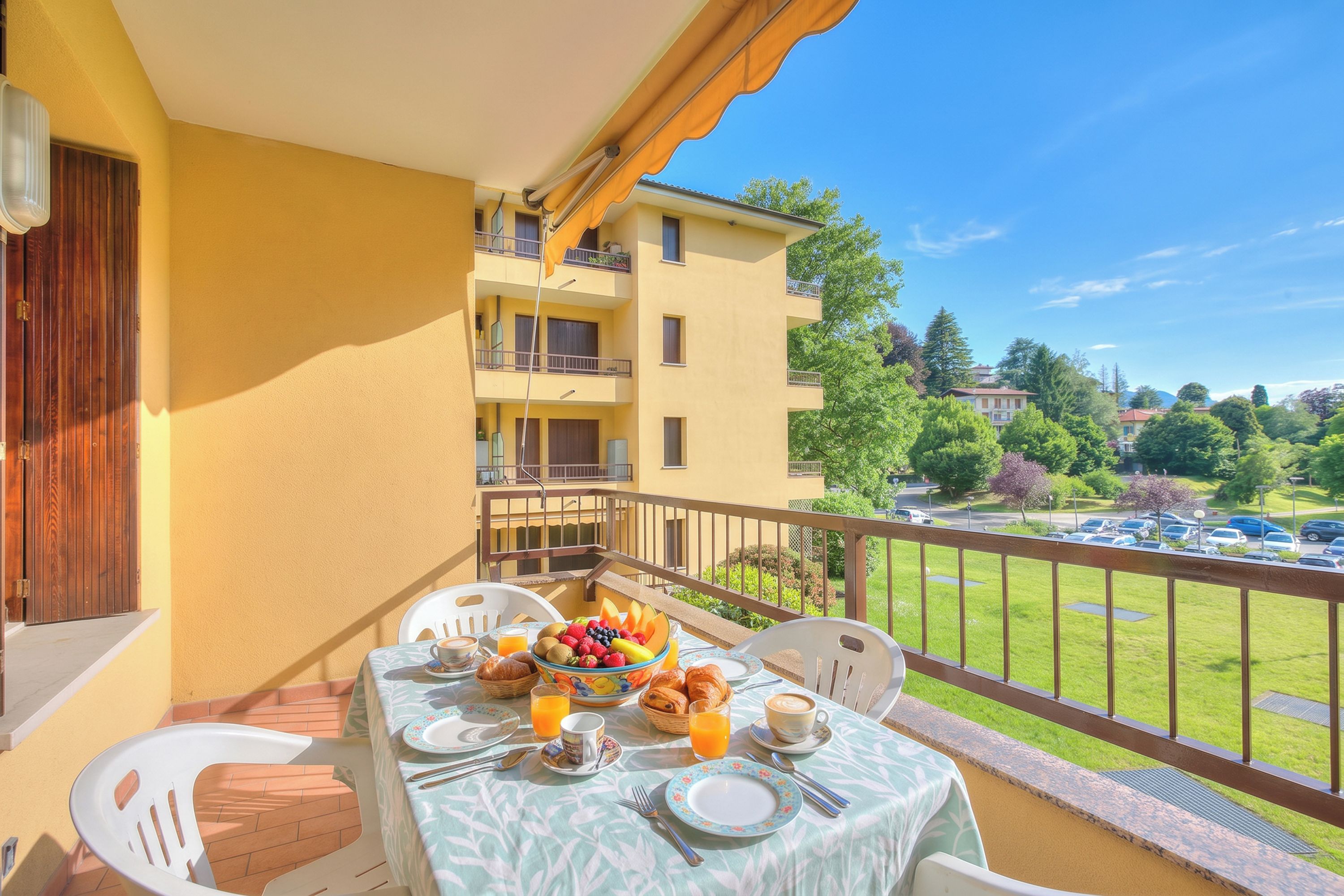 A balcony with a table set for breakfast, including fruits, pastries, and beverages.