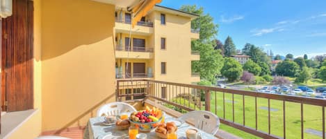 Un balcon avec une table préparée pour le petit-déjeuner, comprenant des fruits, des viennoiseries et des boissons.