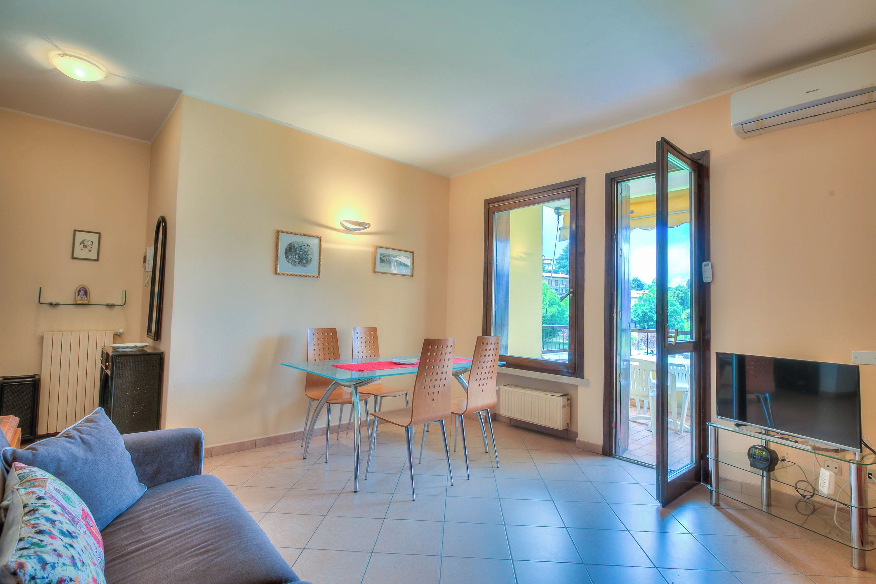 A living room with a sofa, a dining table with chairs, a TV on a stand, and a large window.