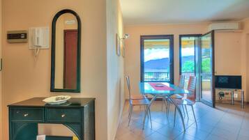 Une pièce comprenant une table à manger, des chaises, un téléviseur, un miroir et donnant sur l’extérieur.