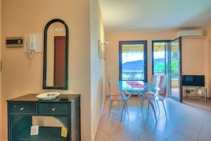 A room with a dining table, chairs, a TV, a mirror, and a view of the outdoors. - Appartamento Lake View Laveno 1br, Sleeps 4 (Laveno Mombello)