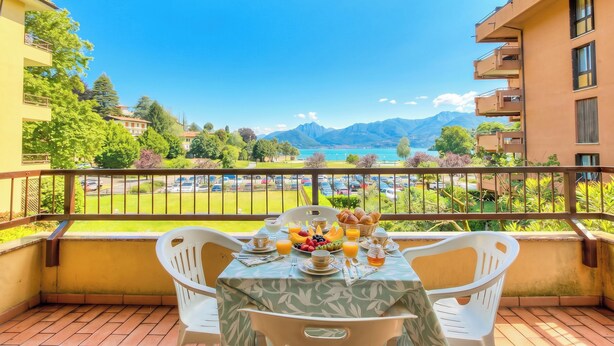 Un balcon avec une table préparée pour le petit-déjeuner, offrant une vue panoramique sur les montagnes et un lac.