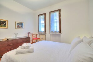 A bedroom with a bed, a dresser, two windows, and two paintings on the wall. - Appartamento Lake View Laveno 1br, Sleeps 4 (Laveno Mombello)