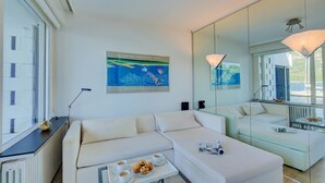 A modern hotel room with a white sofa, a glass coffee table with pastries, a poster of the Australian National Gallery, and a large mirror reflecting the room. - Bellariva On The Lake With View Balcony (Collina d'Oro)